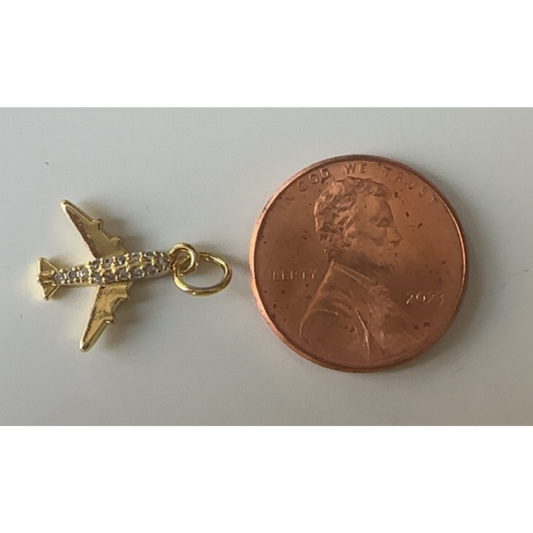 Gold airplane charm next to a penny on a white background