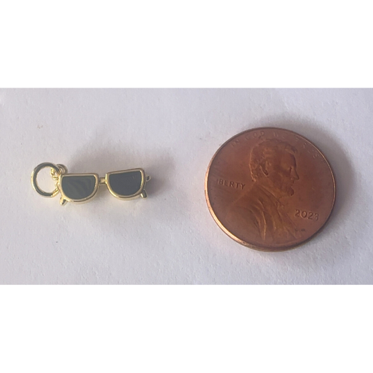 Gold sunglasses charm next to a penny on a white background