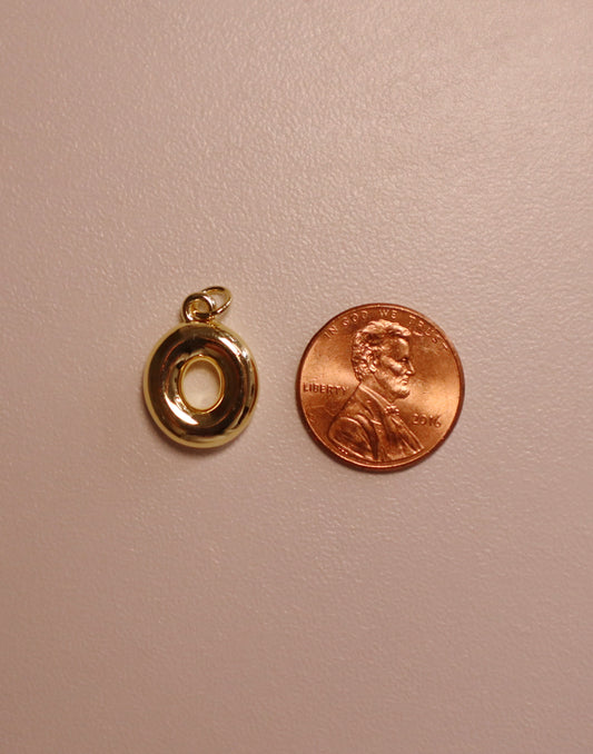 Gold letter pendant next to a penny on a beige background