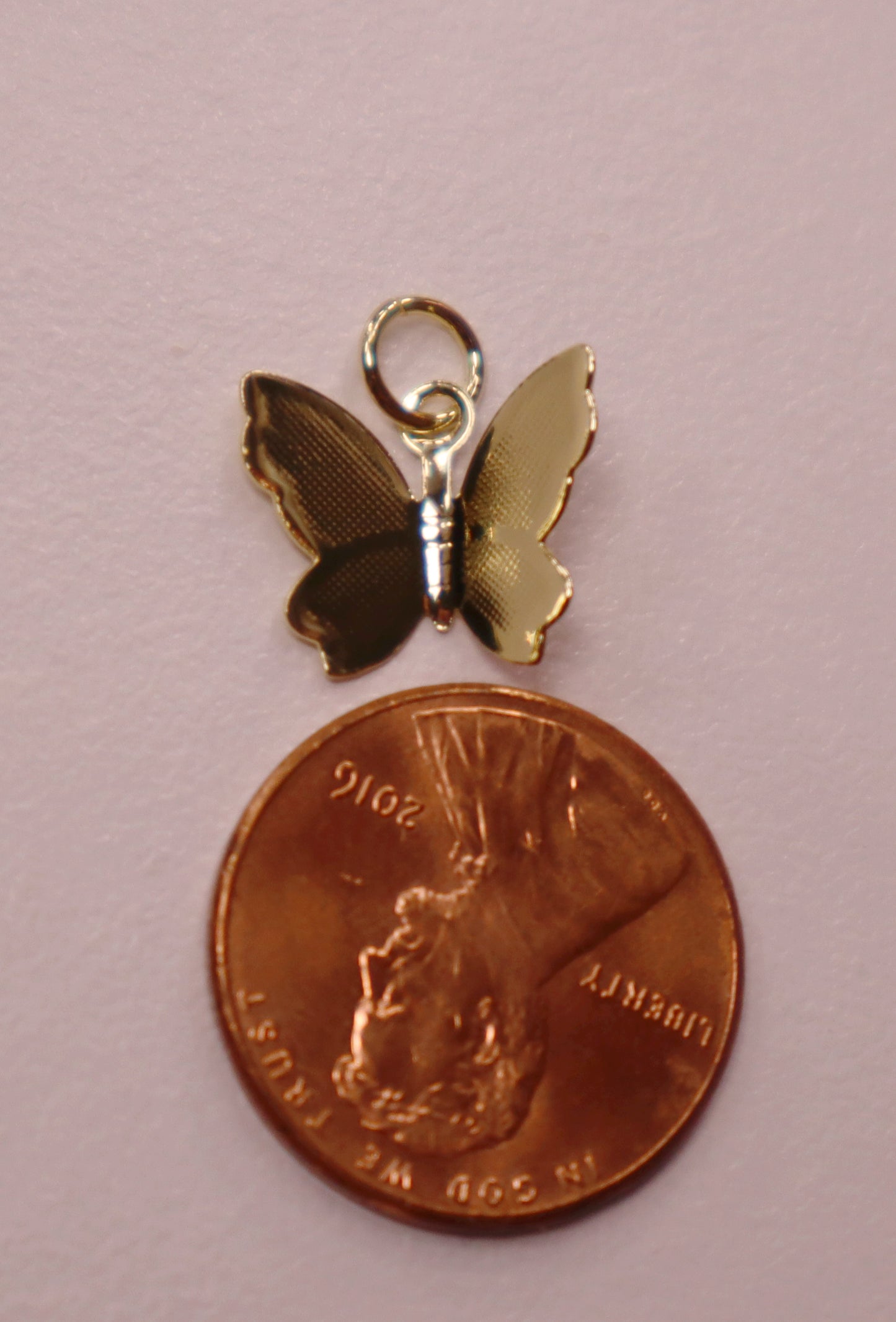 Butterfly charm on a penny against a pink background