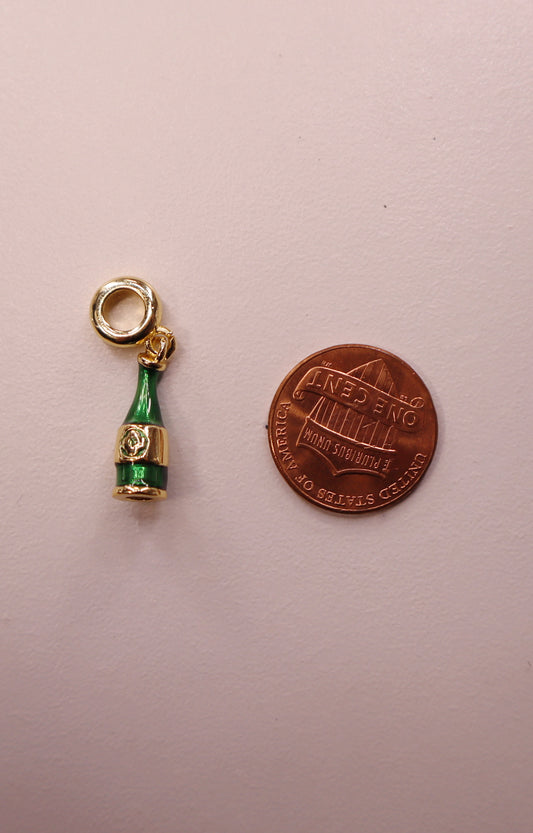 Champagne bottle charm next to a penny on a light pink background