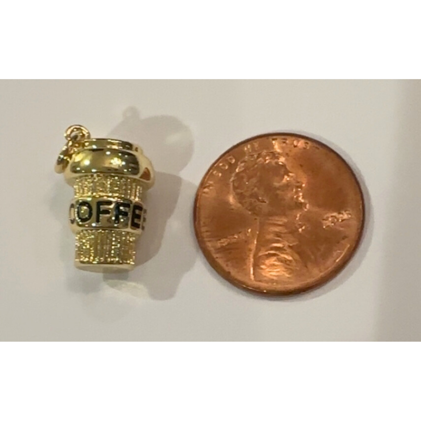 Gold coffee cup charm next to a penny on a white background