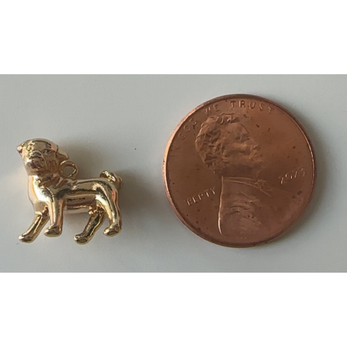Gold dog charm next to a penny on a white background