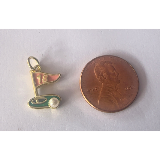 Gold and green golf flag charm next to a penny on a white background