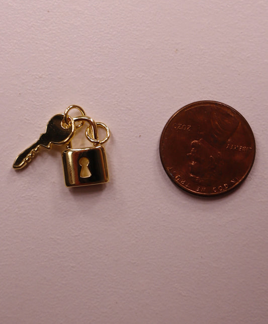Gold key and lock charm next to a penny on a light pink background