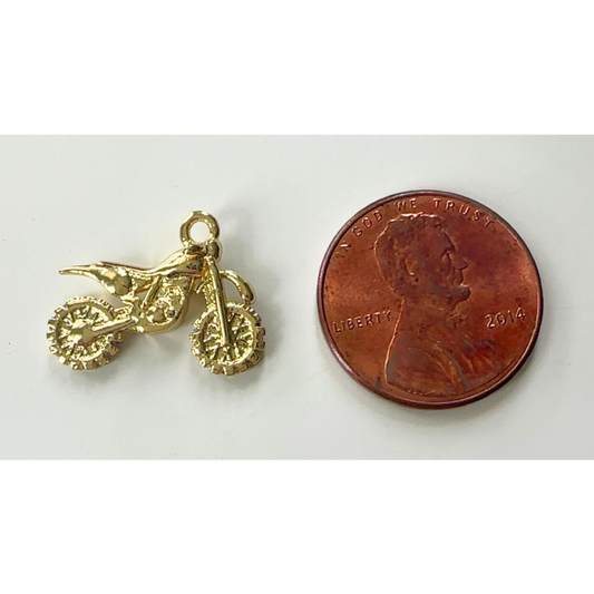Gold dirt bike charm next to a penny on a white background