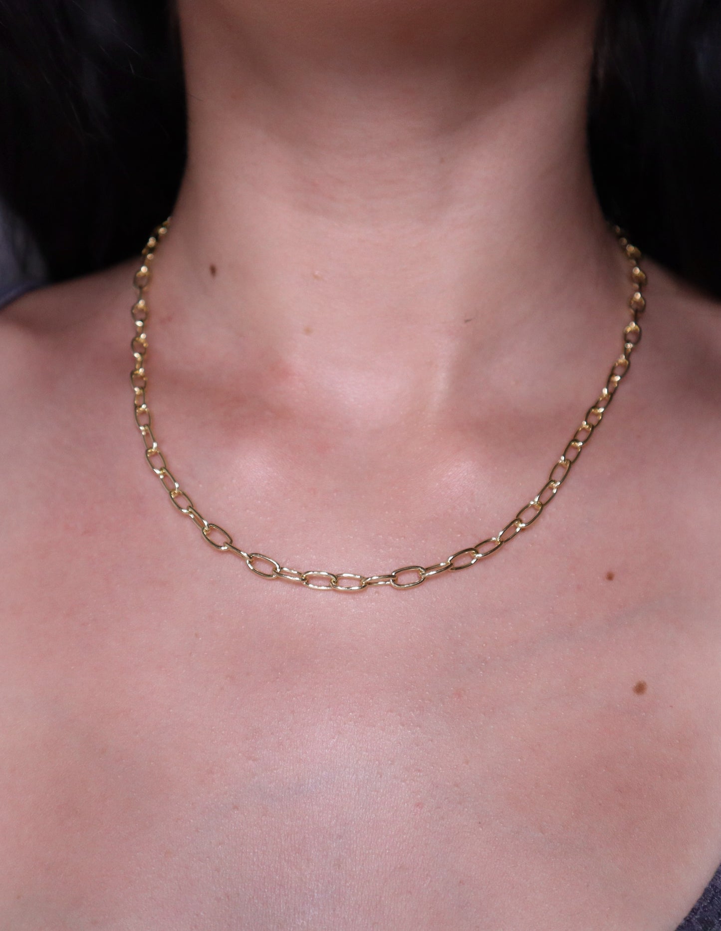 Gold oval necklace on a person's neck with a dark background