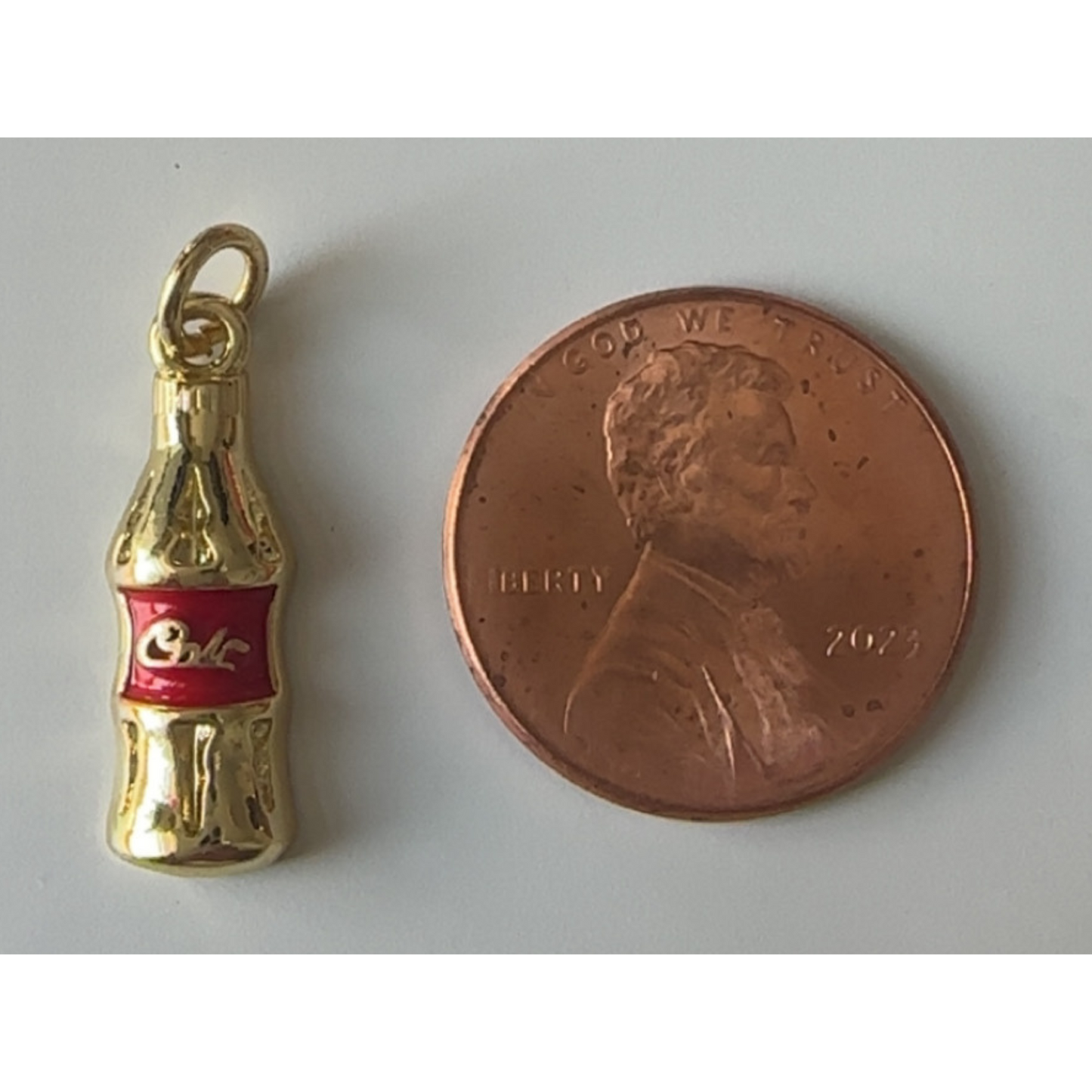 Gold Coca-Cola bottle charm next to a penny on a white background