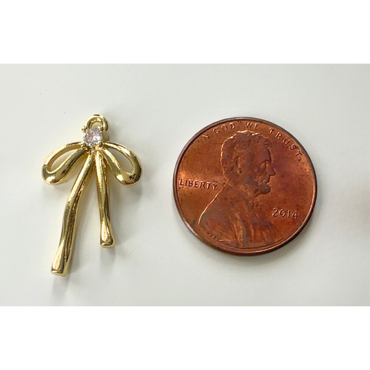 Gold bow-shaped pendant next to a penny on a white background