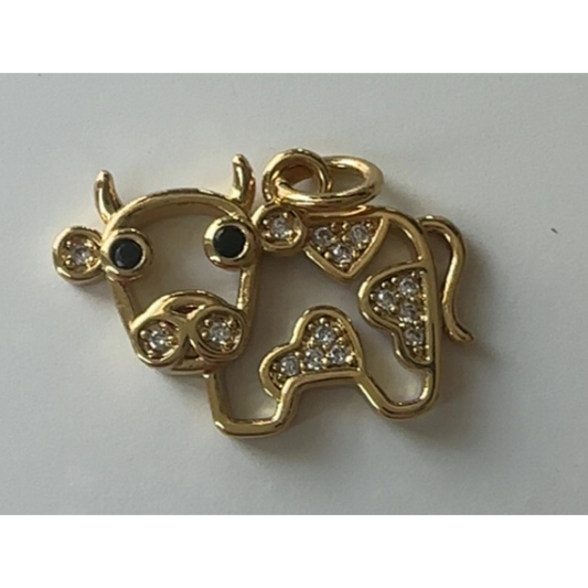 Gold cow pendant with black eyes and clear stones on a light gray background