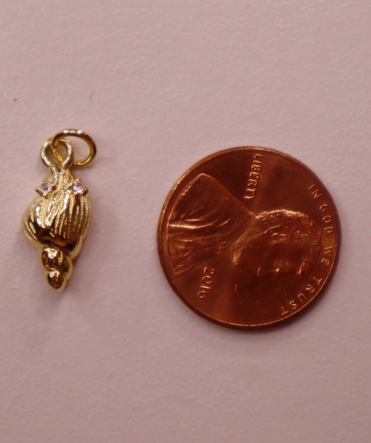 Gold shell charm next to a penny on a pink background