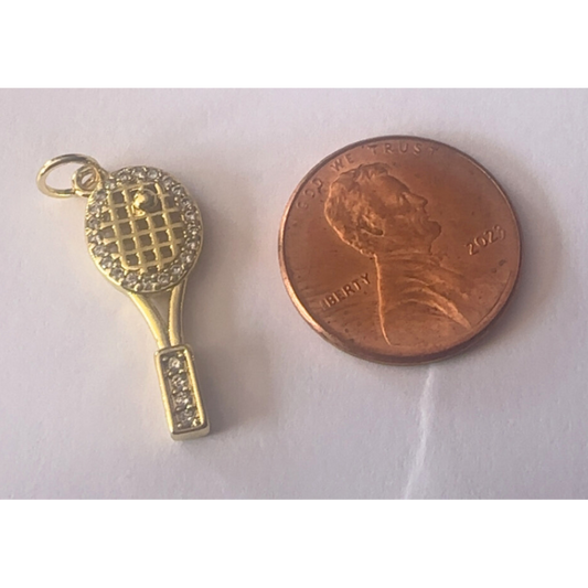 Gold tennis racket charm next to a penny on a white background