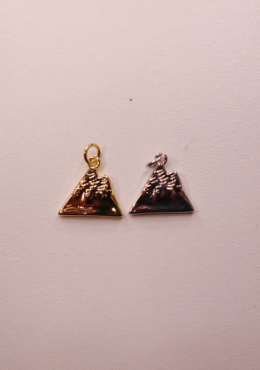 Two mountain charms, one gold and one silver, on a light gray background