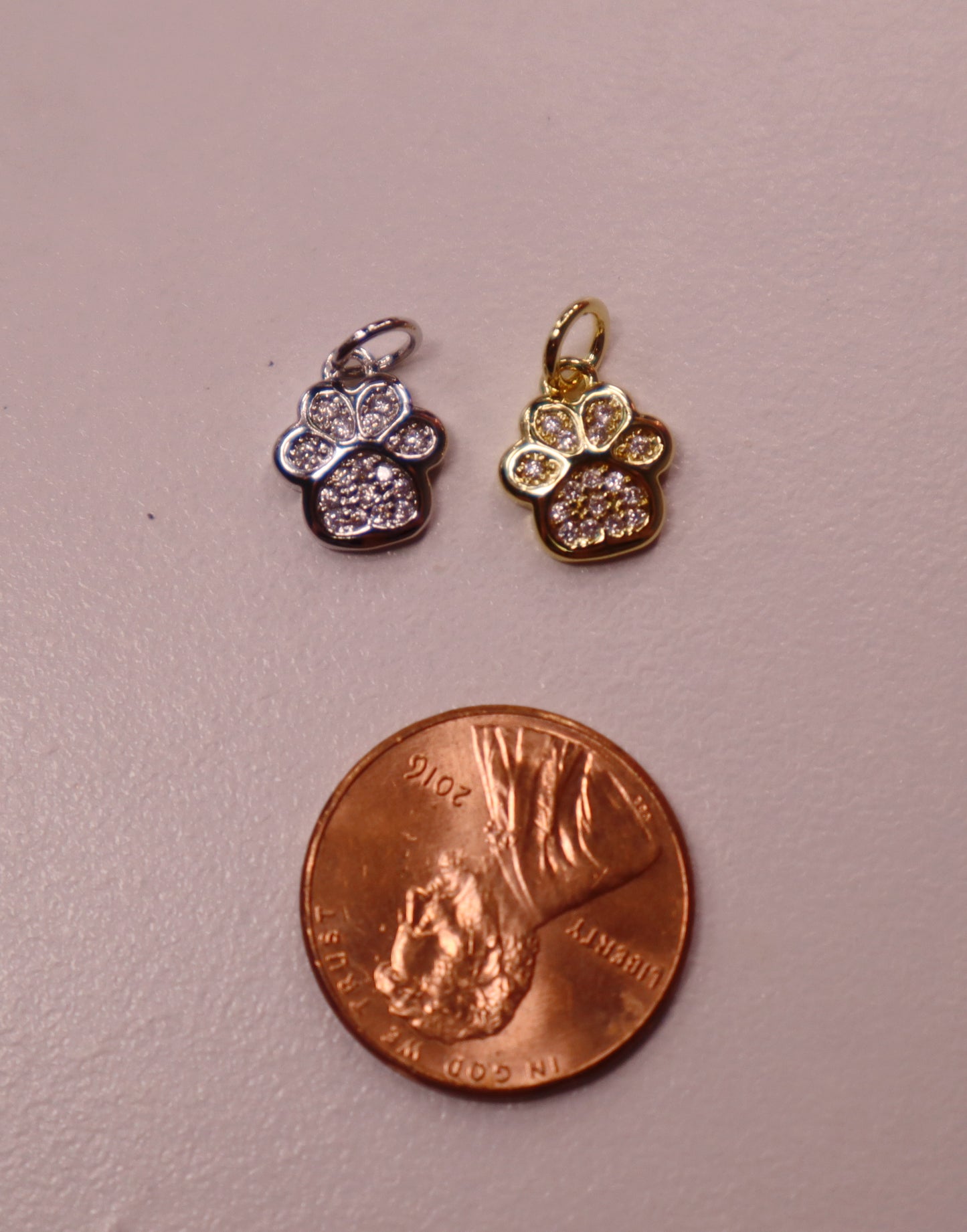 Two small gold and silver paw pendants on a penny for scale.