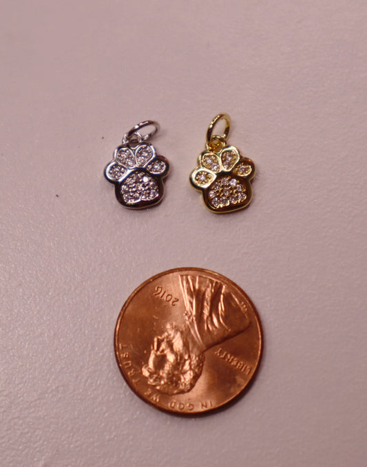Two small gold and silver paw pendants on a penny for scale.