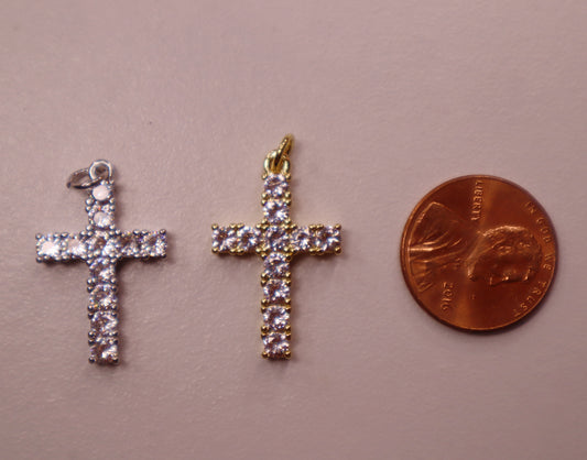 Two cross-shaped pendants next to a penny on a beige background