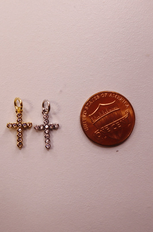 Two cross-shaped pendants next to a penny on a light gray background