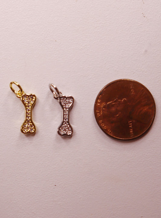 Two gold bone-shaped charms next to a penny on a white background