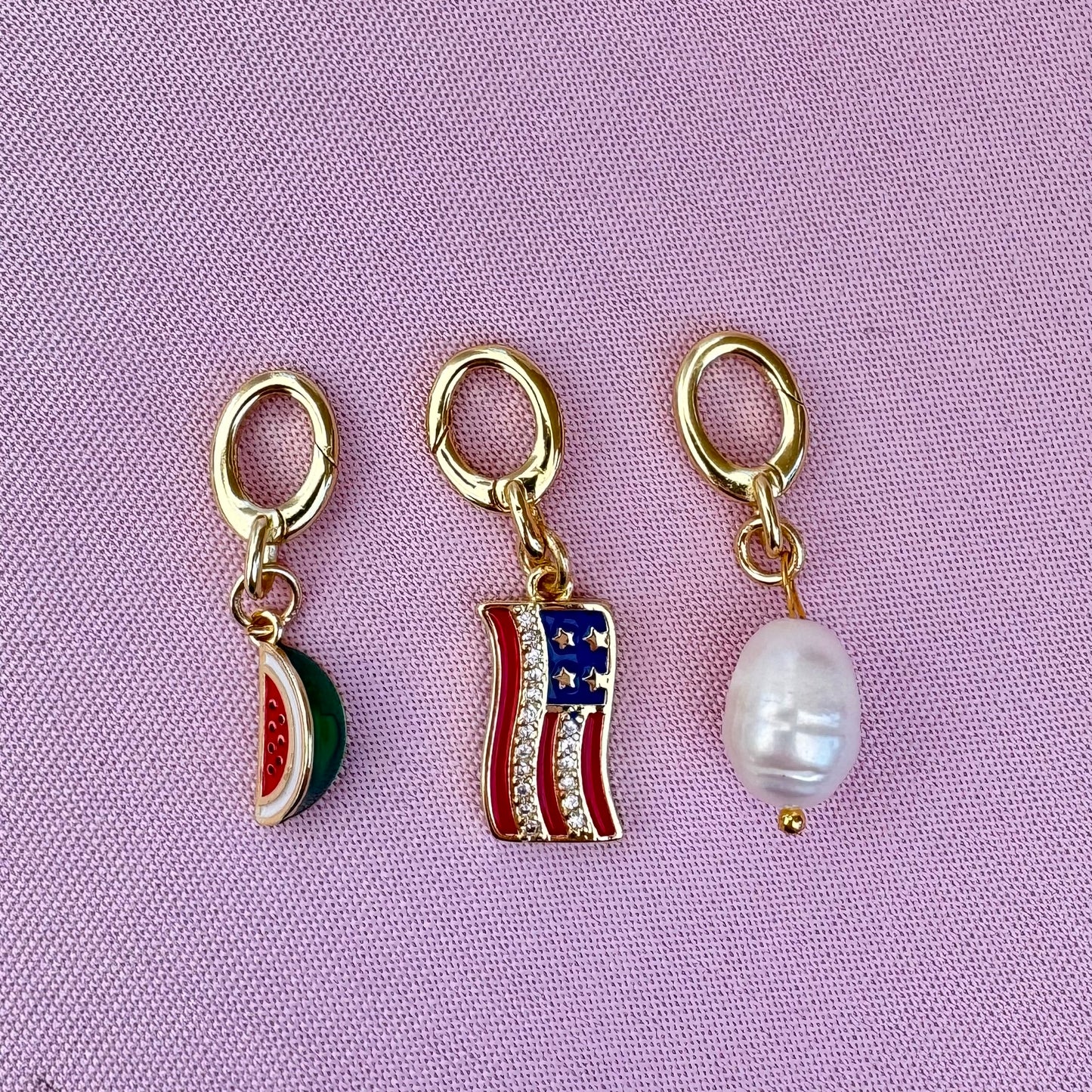 Three gold bikini charm pendants on a pink background