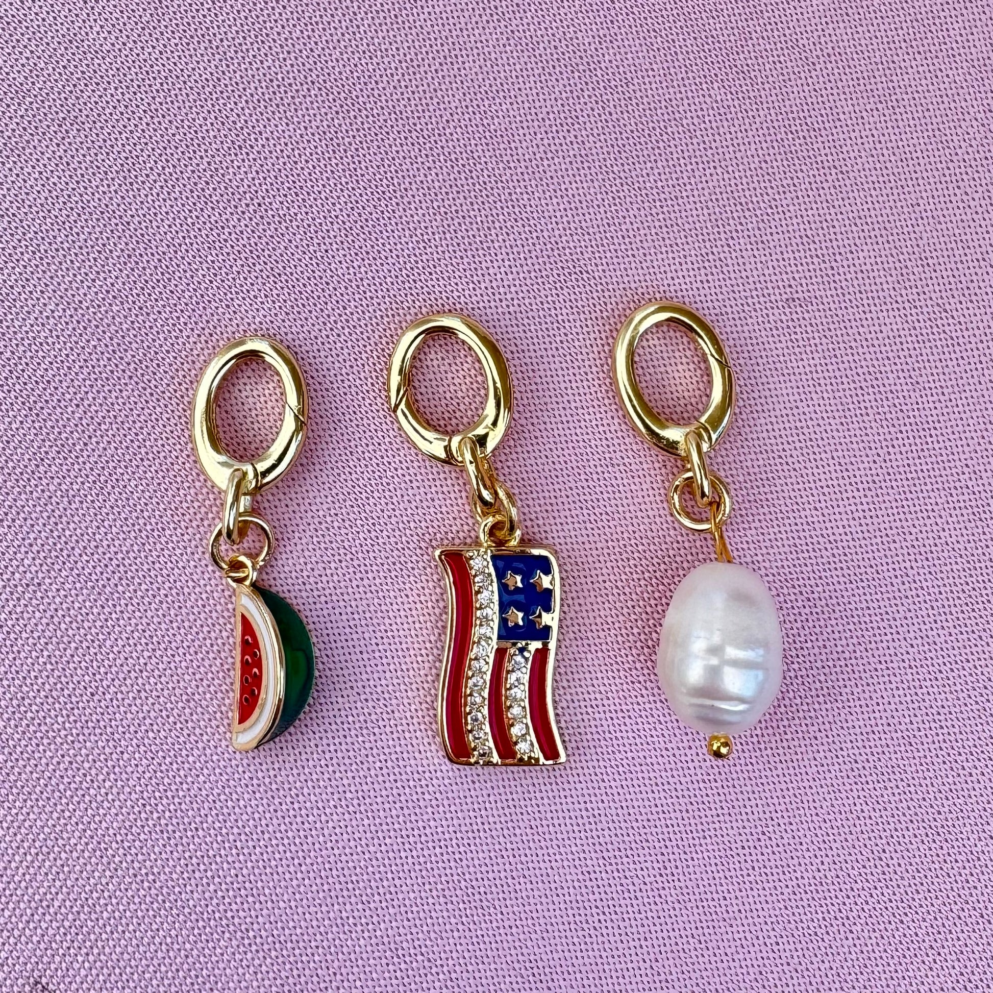 Three gold bikini charm pendants on a pink background