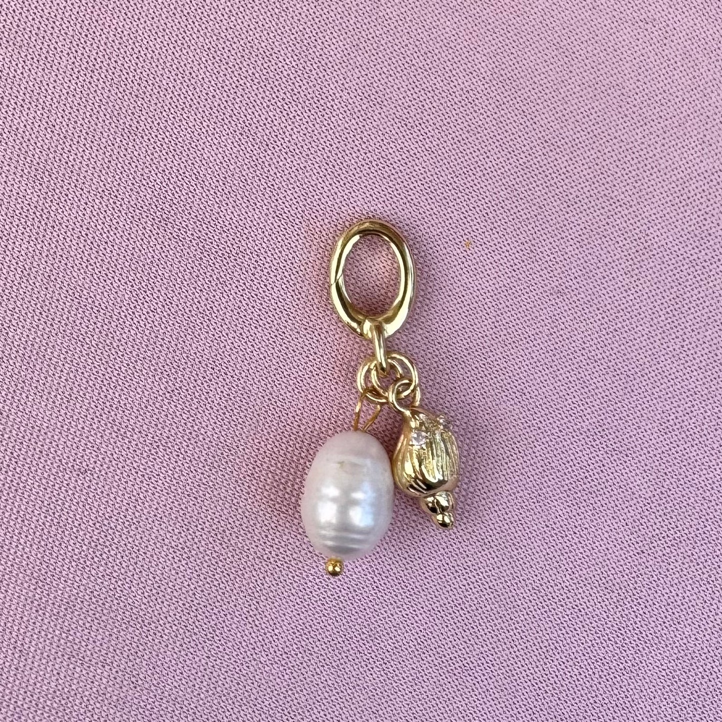 Gold charm with a pearl on a pink background