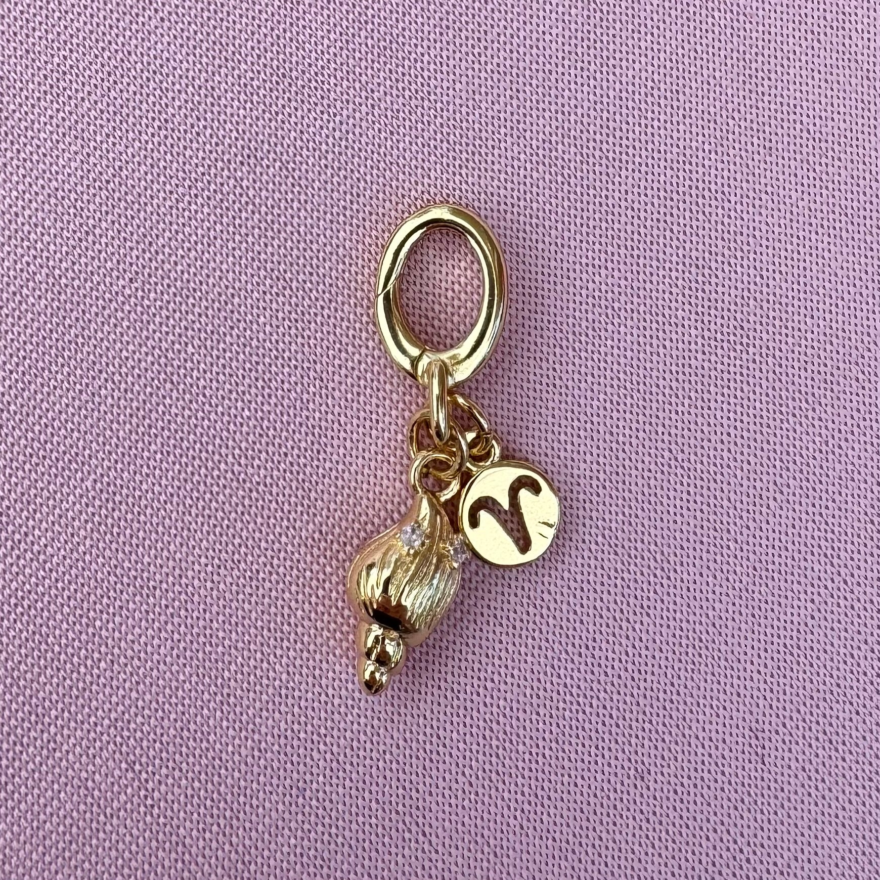 Gold charm with a small ball and a zodiac charm on a purple background