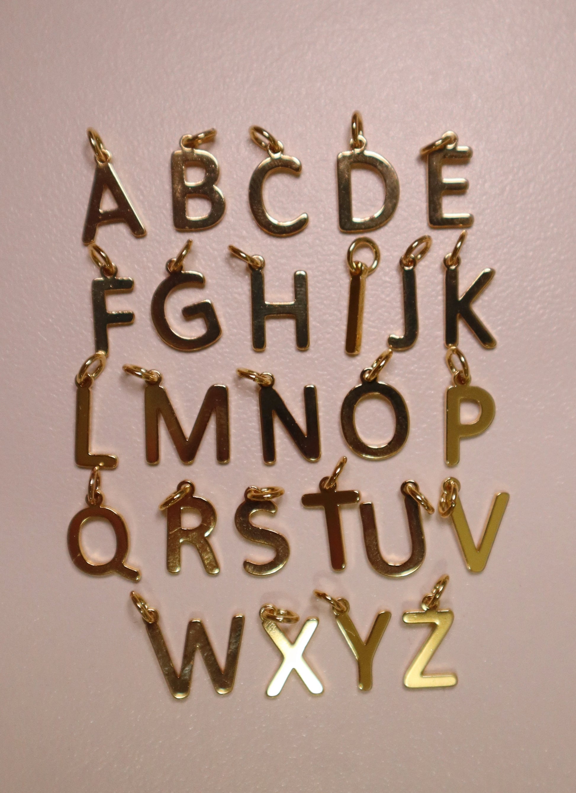 Gold letter charms from A to Z on a pink background