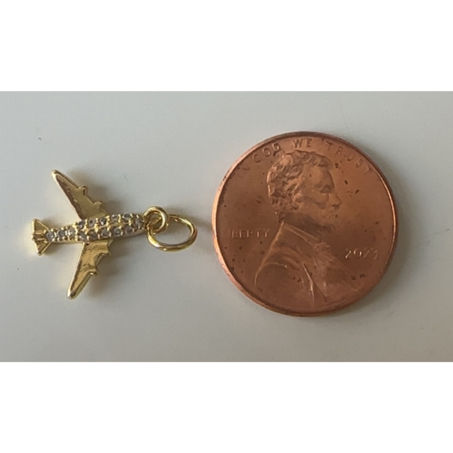 Gold airplane charm next to a penny on a white background