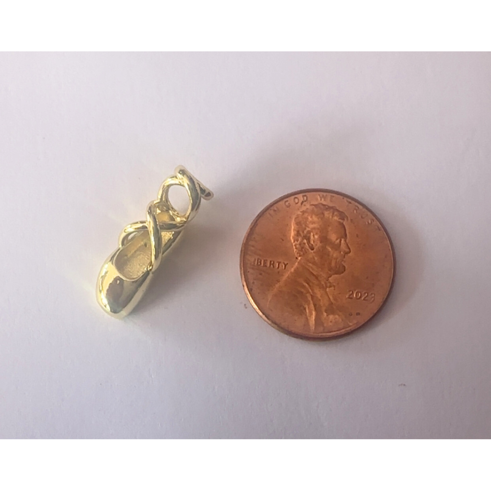 Gold ballet shoe pendant next to a penny on a white background