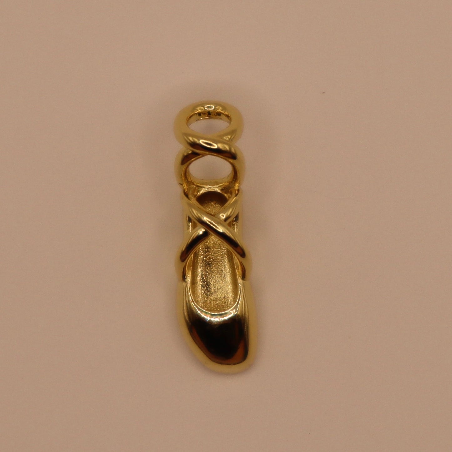 Gold ballet slipper charm on a beige background