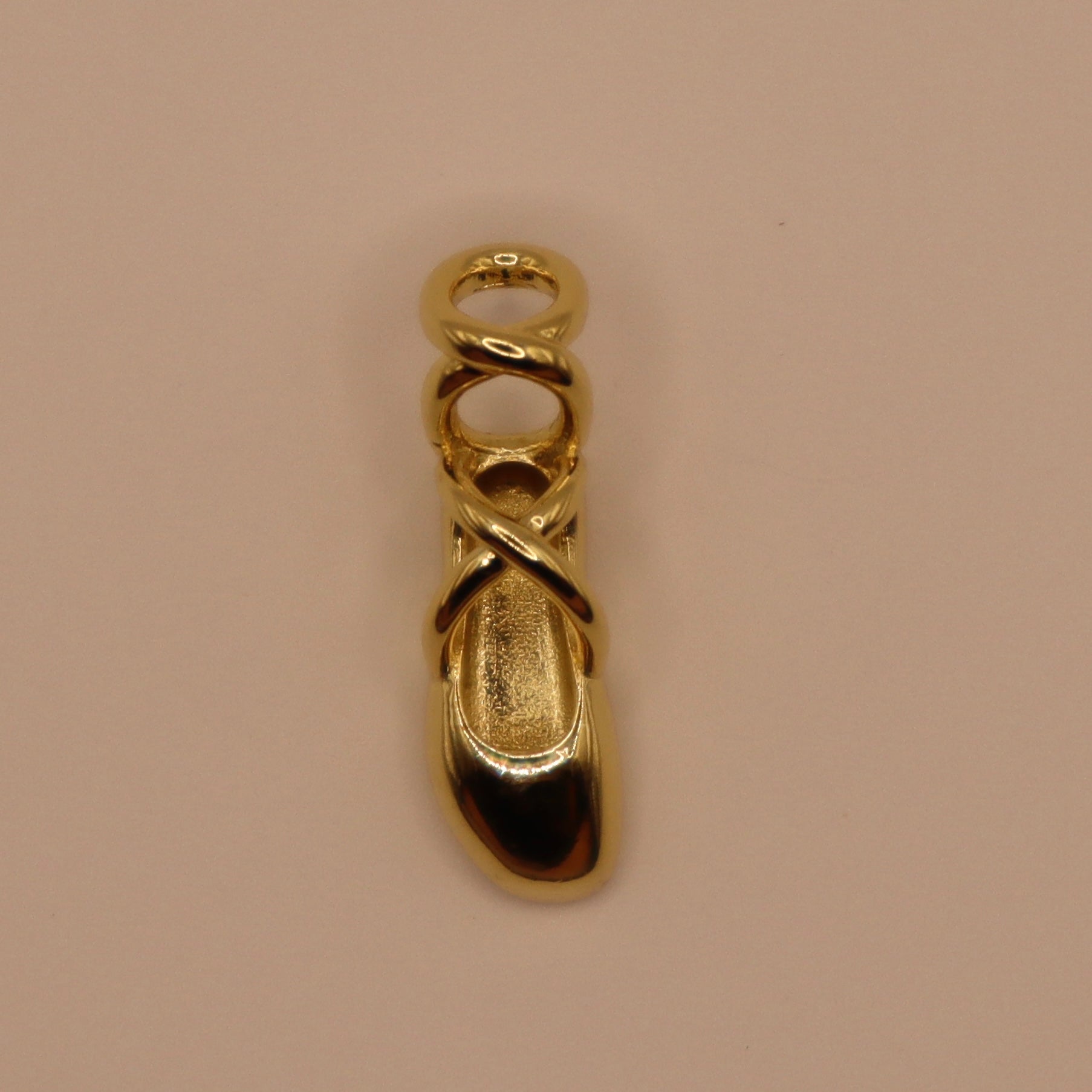 Gold ballet slipper charm on a beige background
