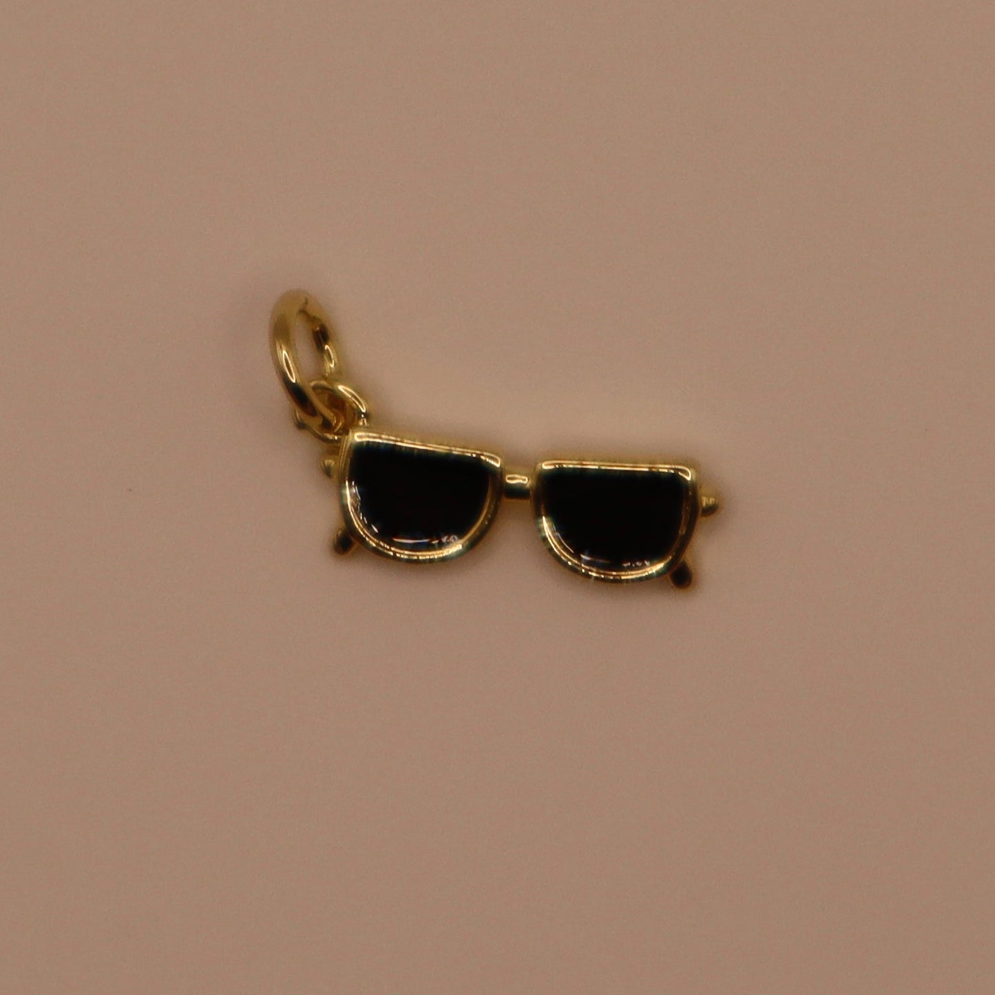Gold sunglasses charm on a beige background