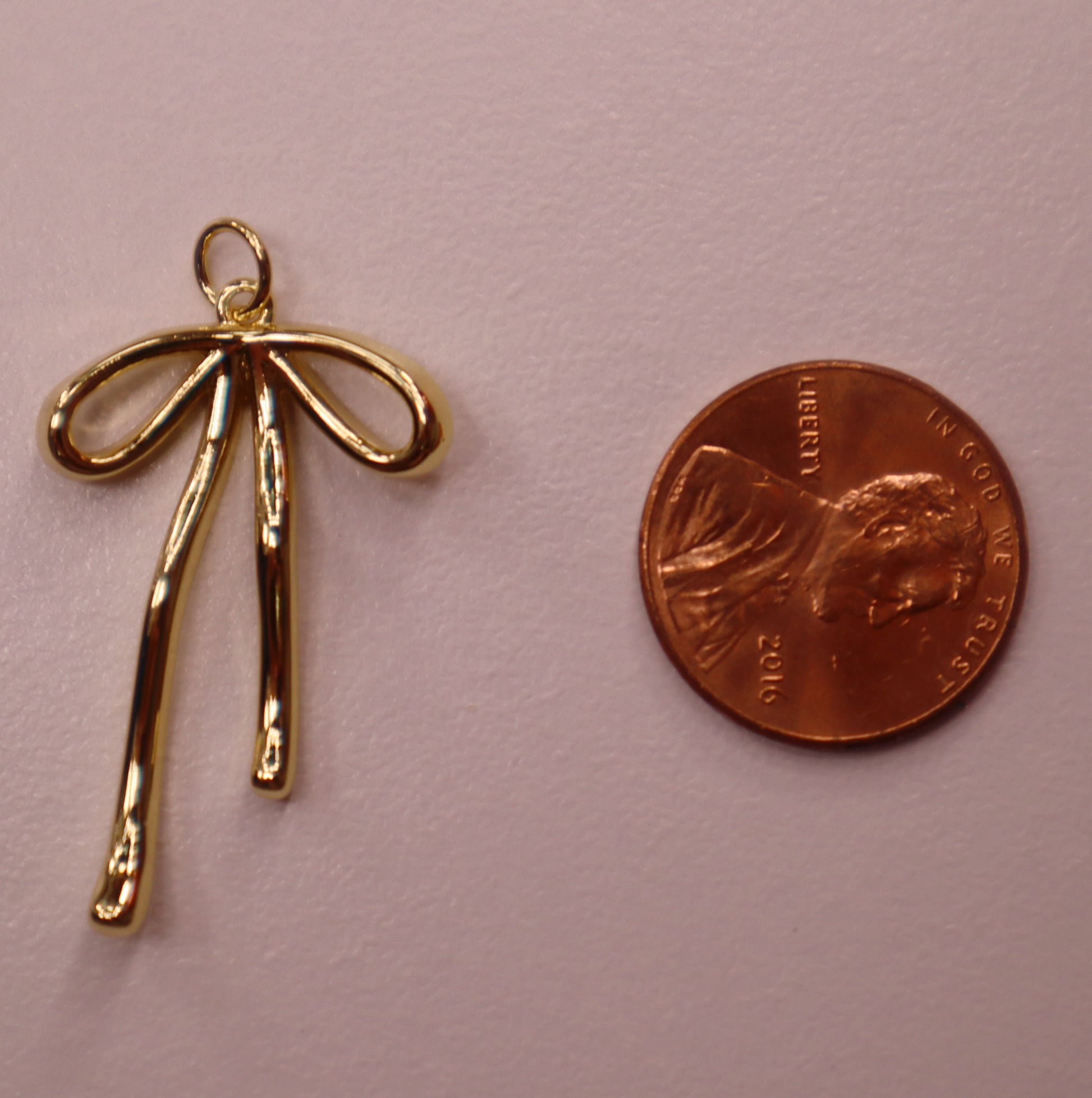 Gold bow-shaped pendant next to a penny on a pink background