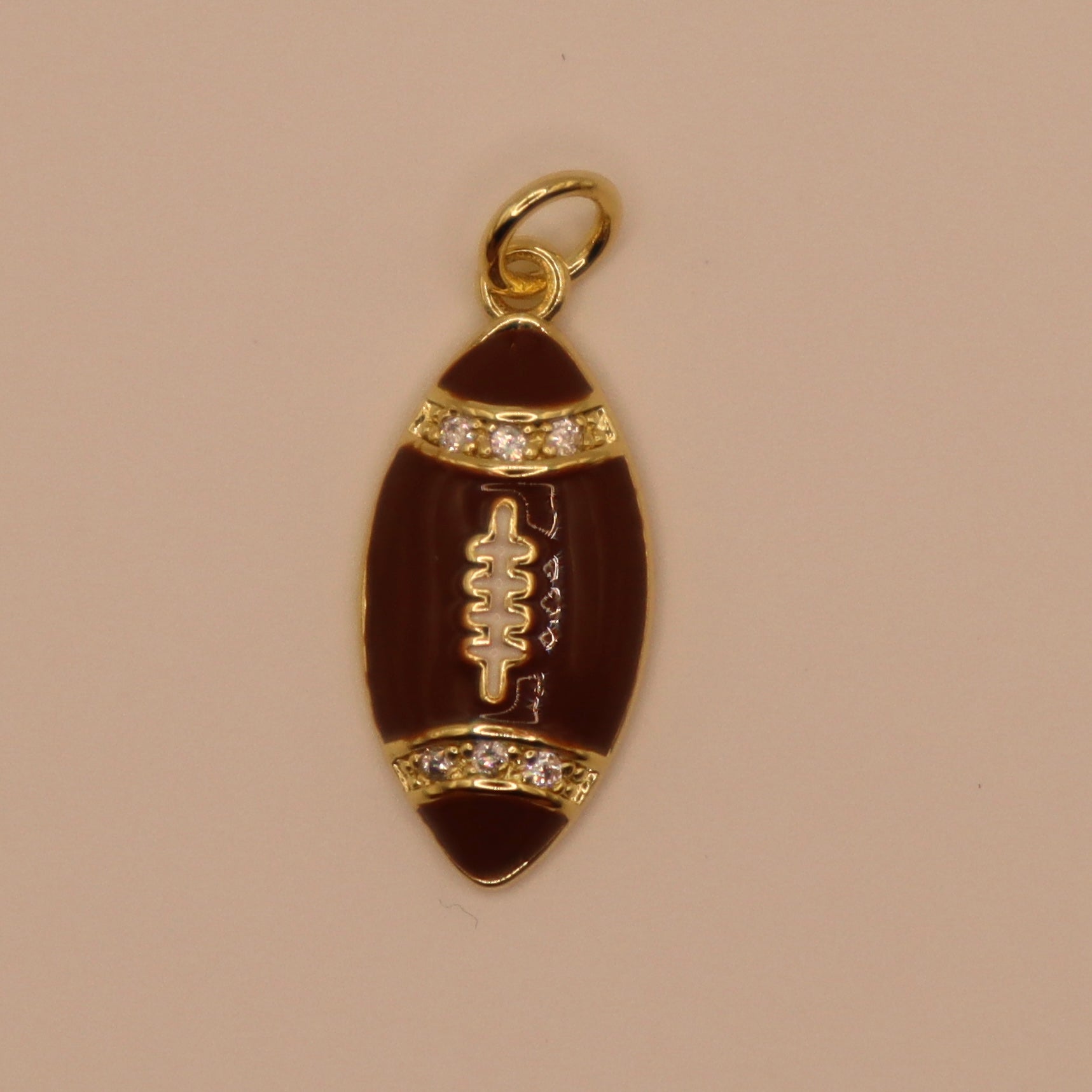 Gold and brown football-shaped pendant with embedded stones on a beige background