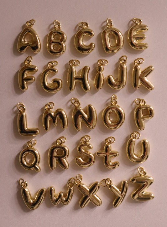 Gold letter pendants arranged in a grid on a pink background