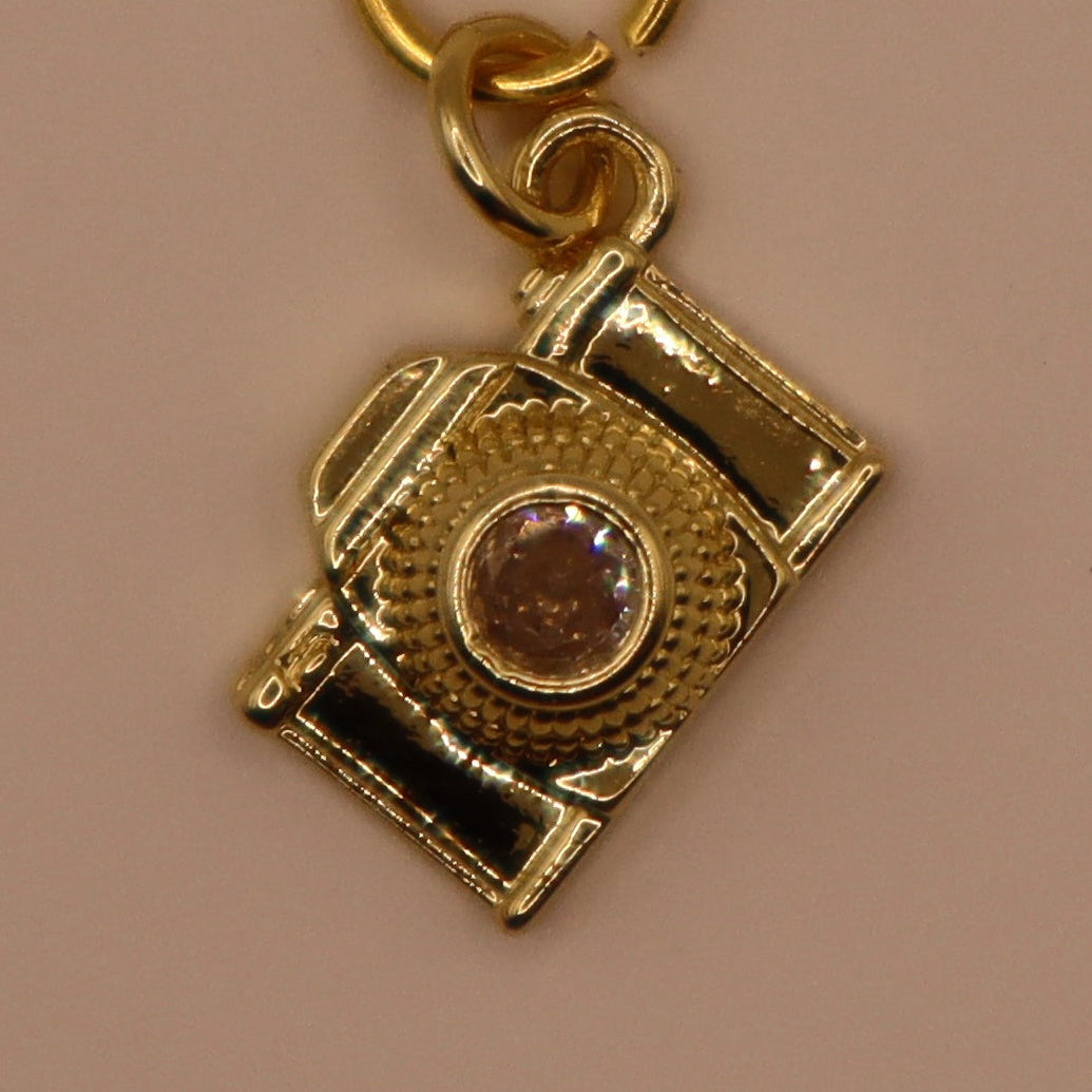 Gold camera-shaped charm on a beige background