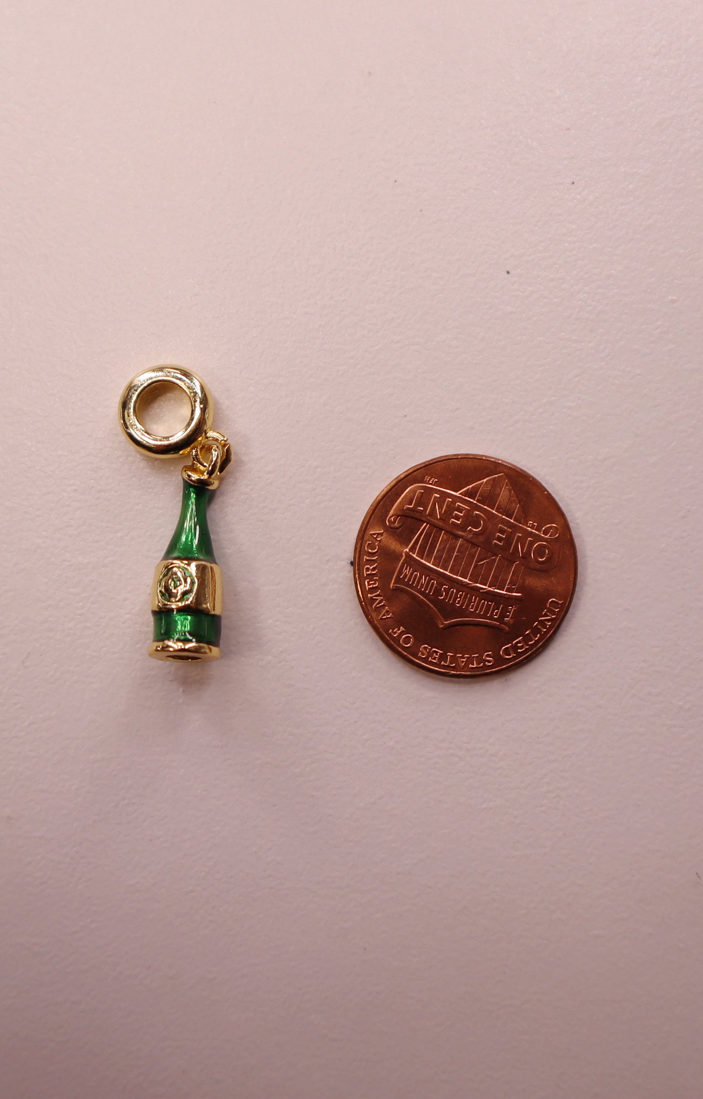 Champagne bottle charm next to a penny on a light pink background