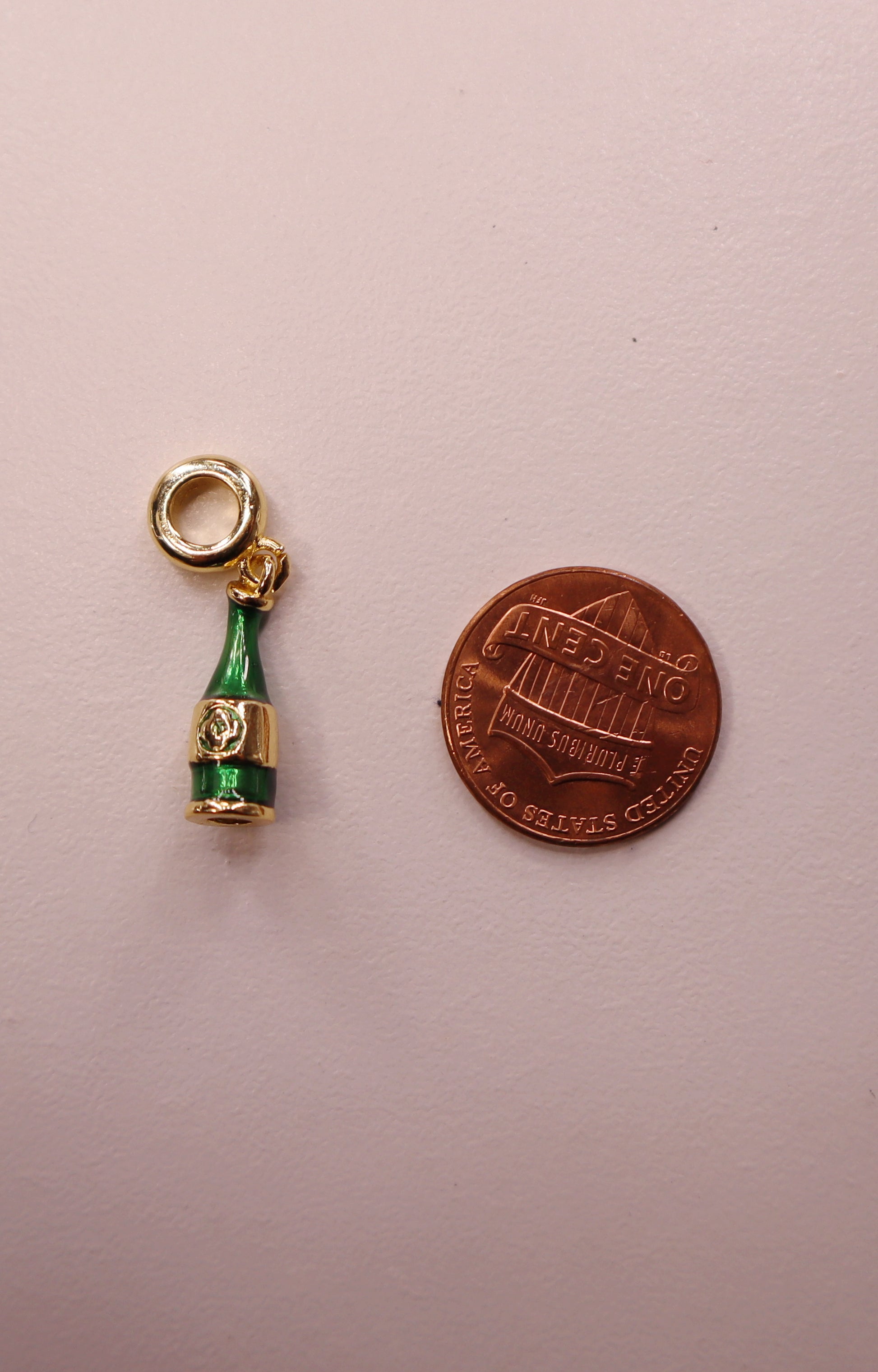 Champagne bottle charm next to a penny on a light pink background