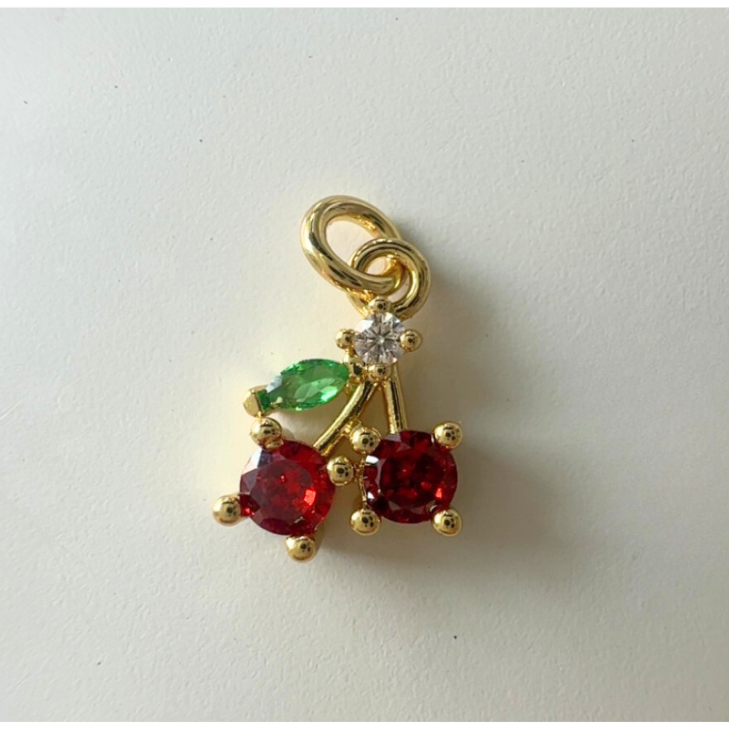 Gold cherry charm with red and green gemstones on a white background