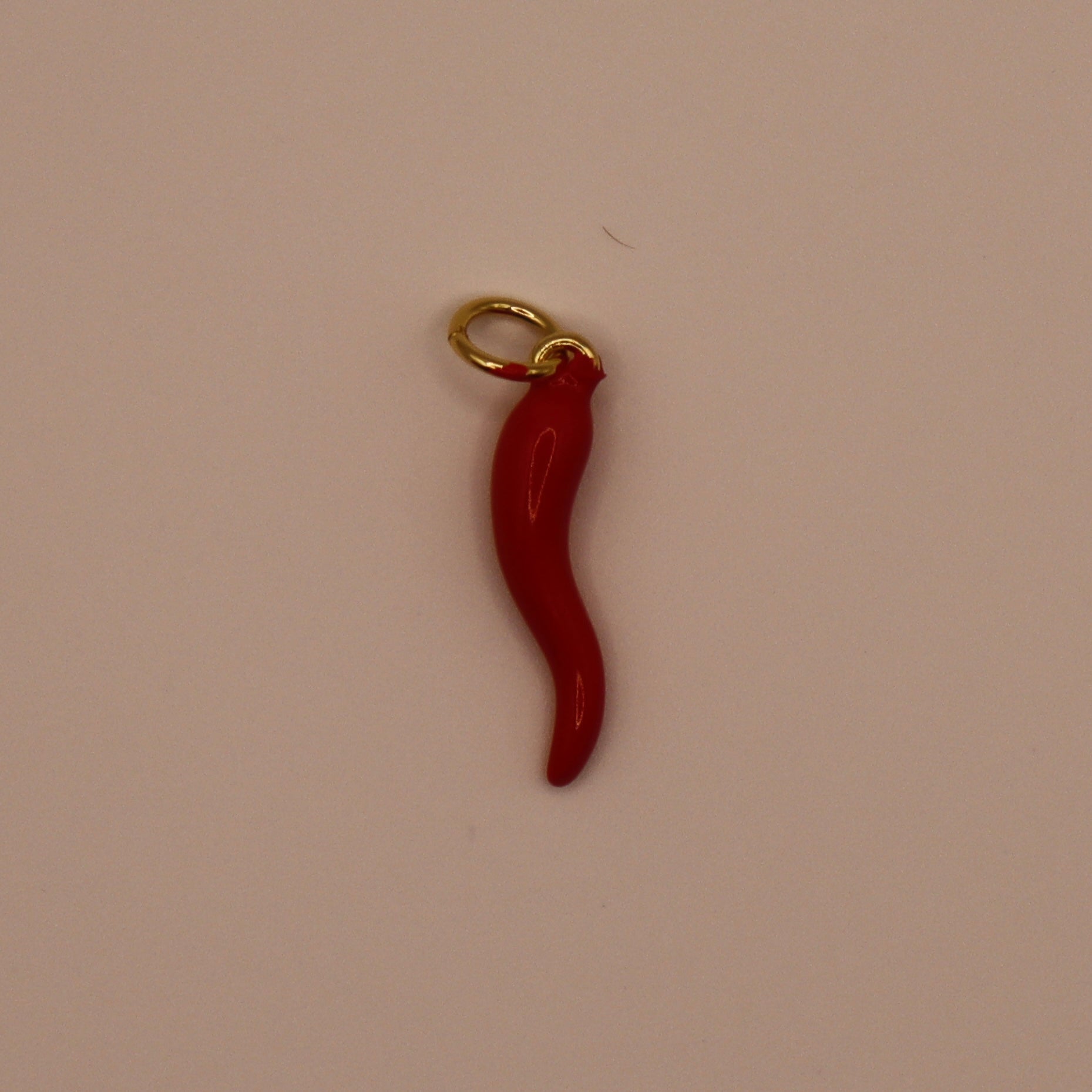 Red chili pepper charm with gold loop on a beige background