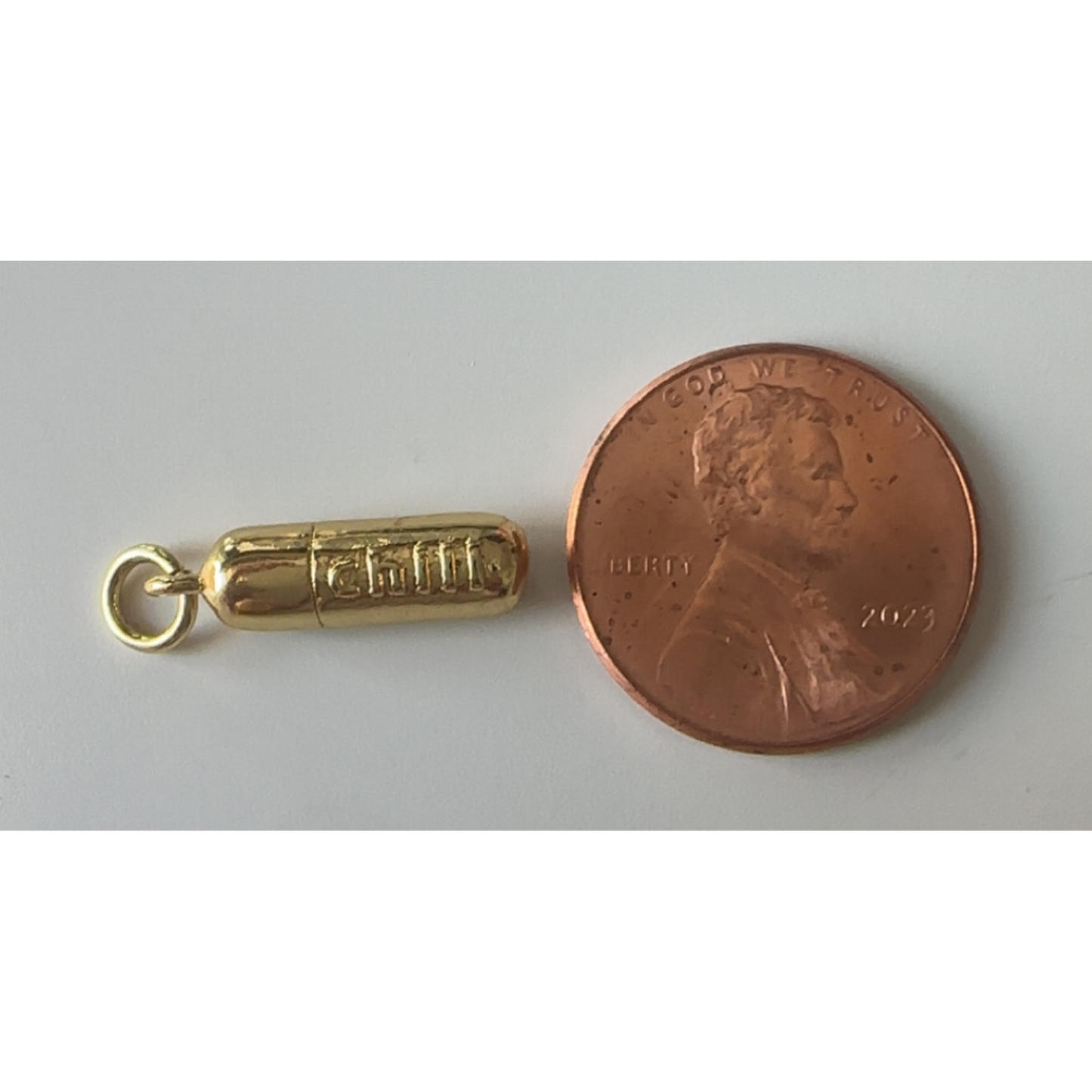 Gold charm next to a penny on a gray background