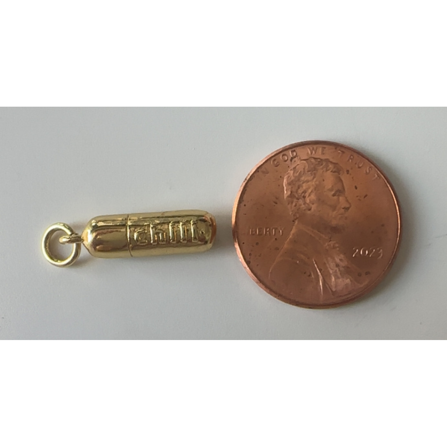 Gold charm next to a penny on a gray background