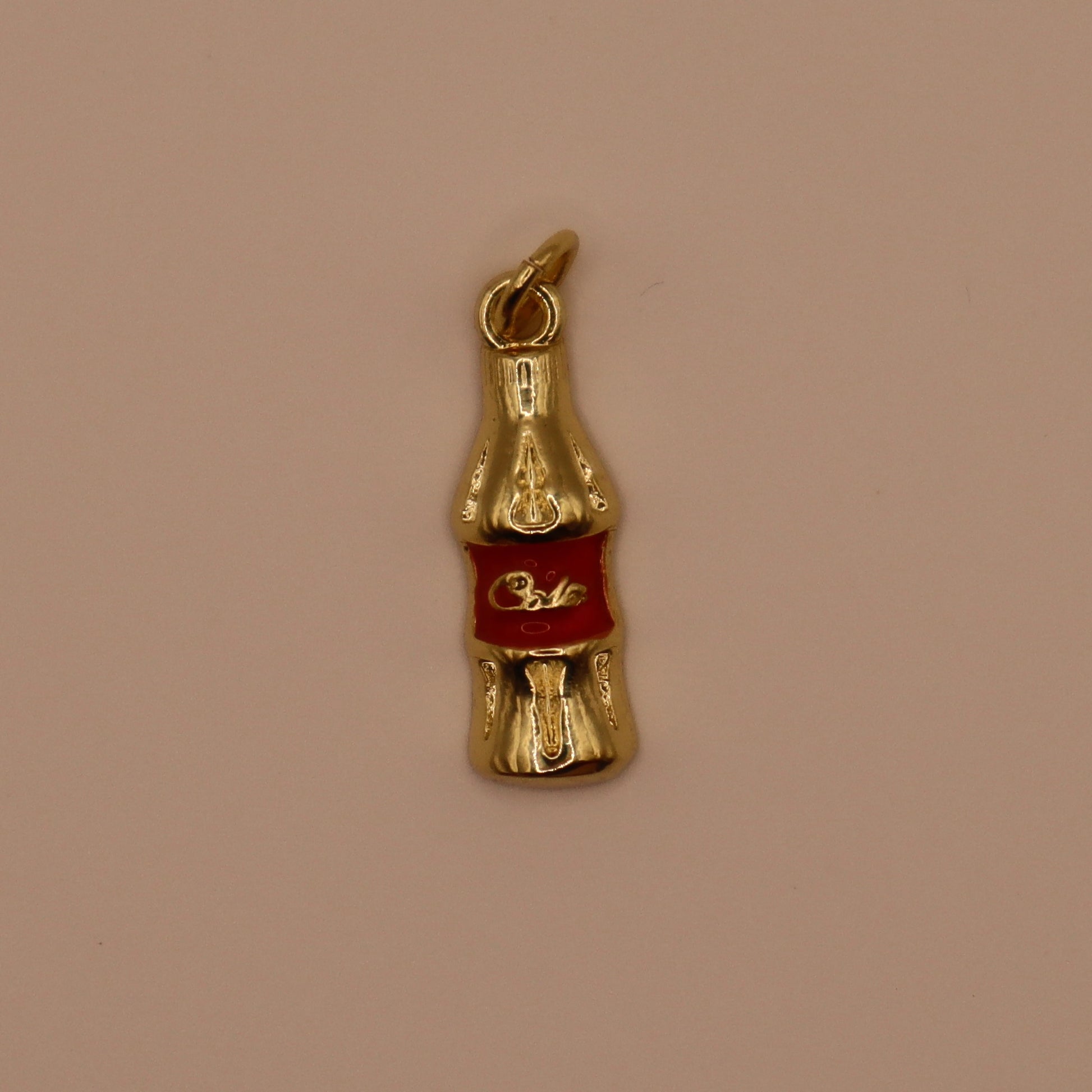 Gold Coca-Cola bottle charm on a beige background
