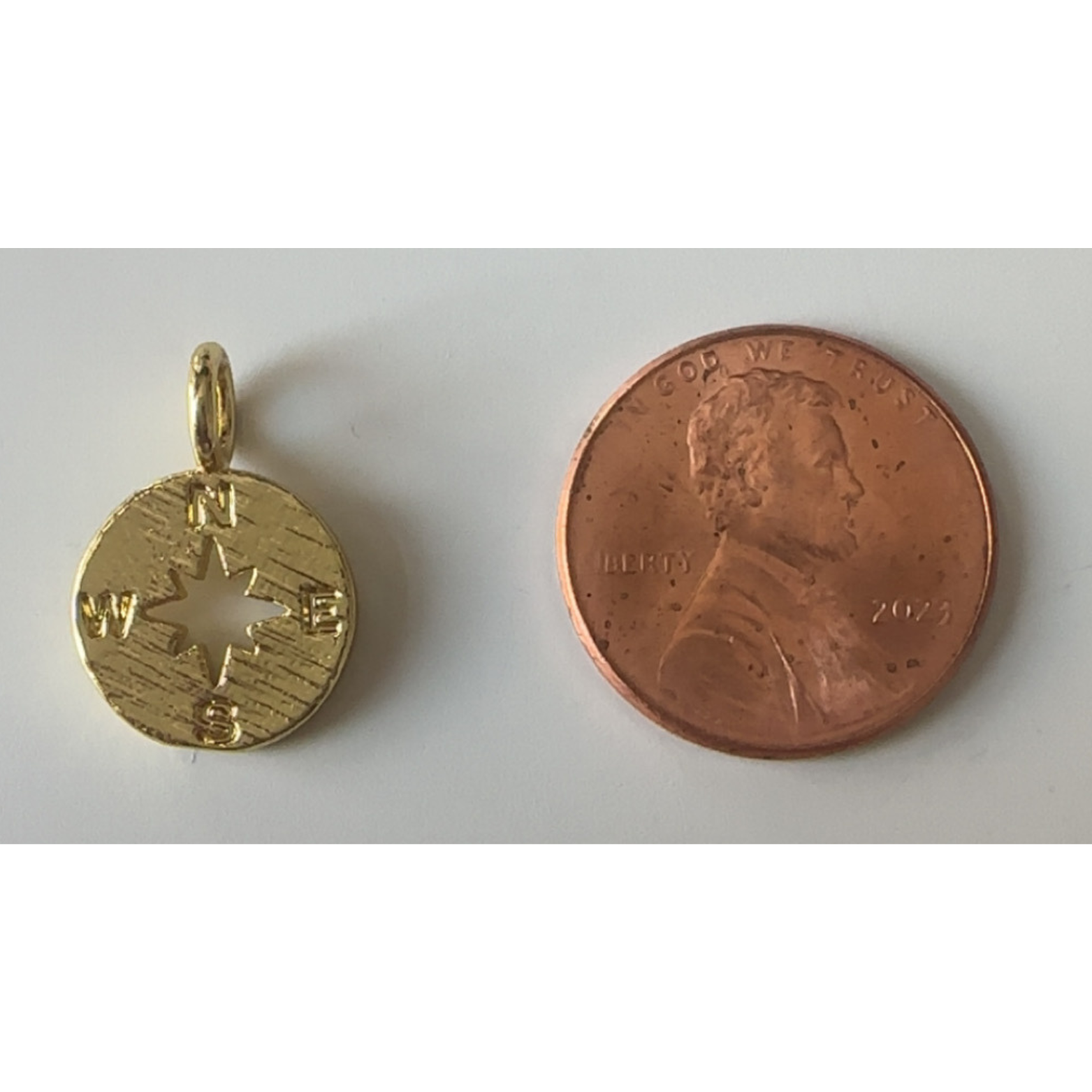 Gold compass pendant and copper penny on a white background