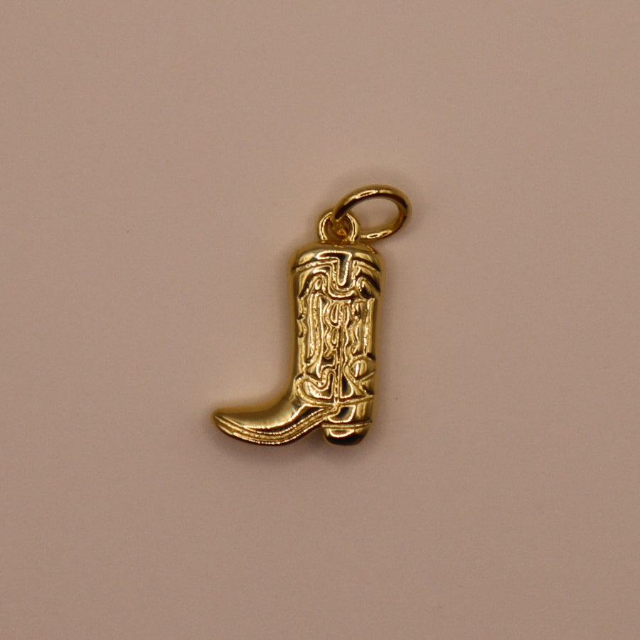 Gold cowgirl boot charm on a beige background
