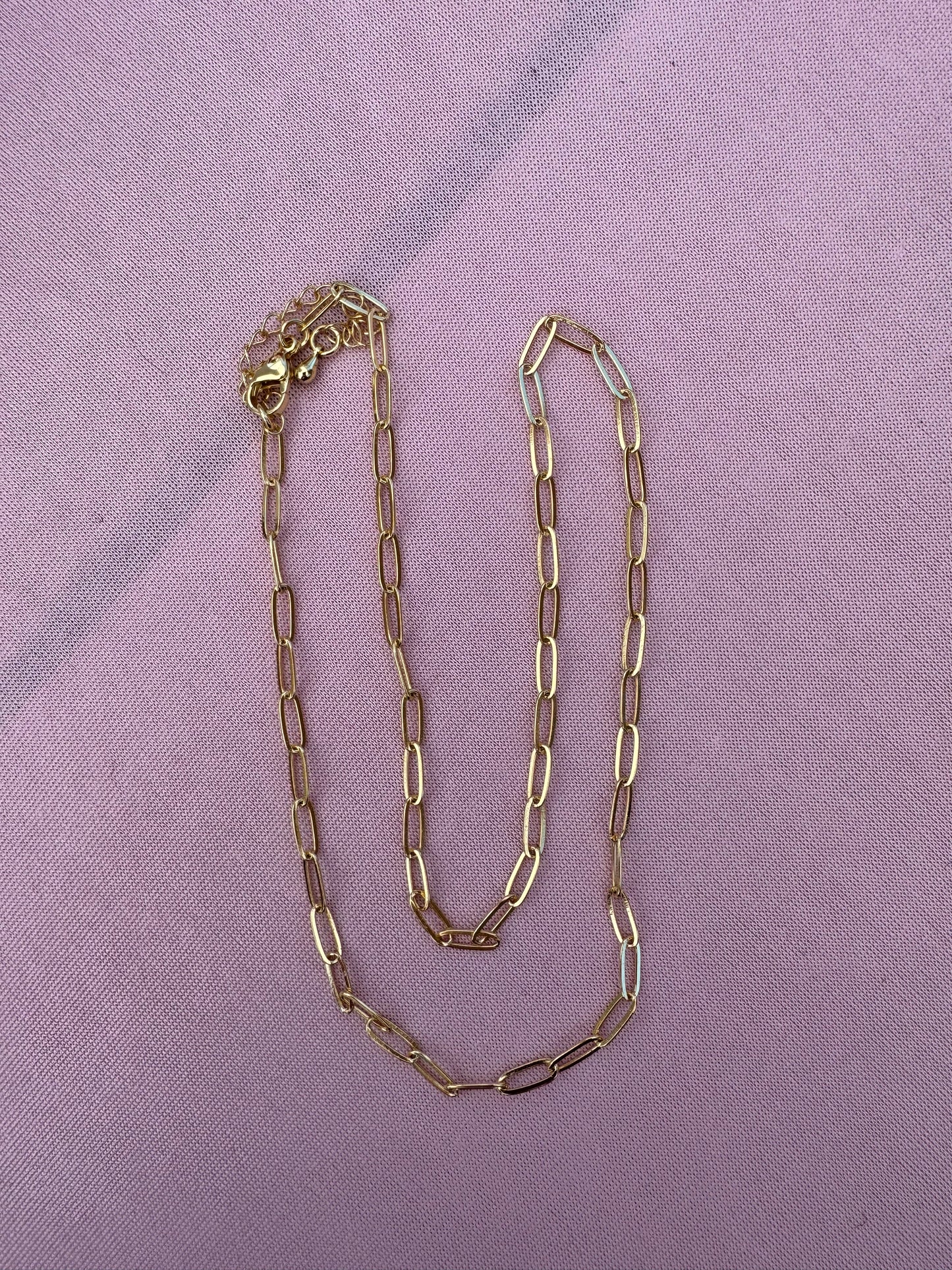 Gold dainty paperclip chain necklace on a purple fabric background