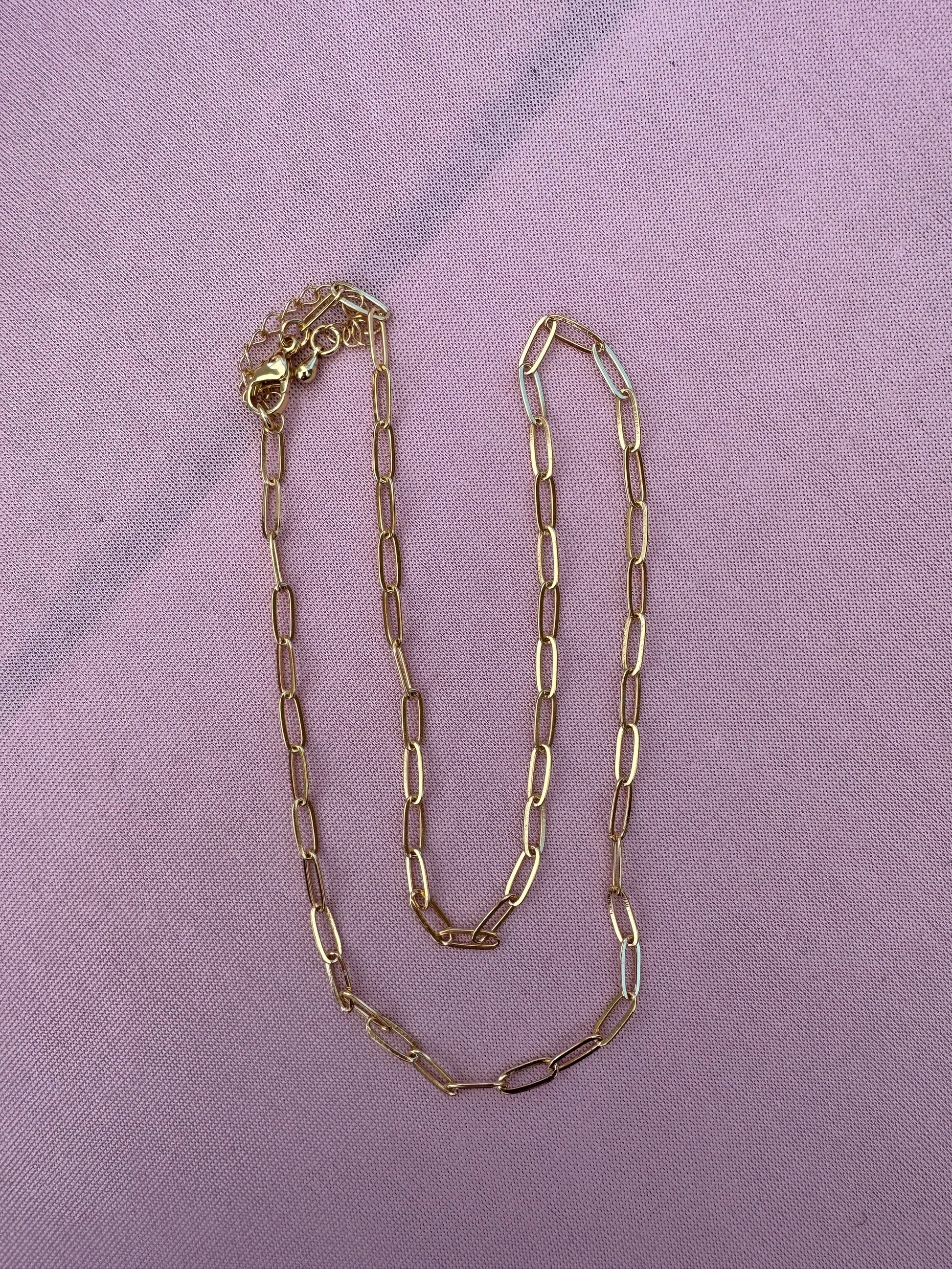 Gold dainty paperclip chain necklace on a purple fabric background