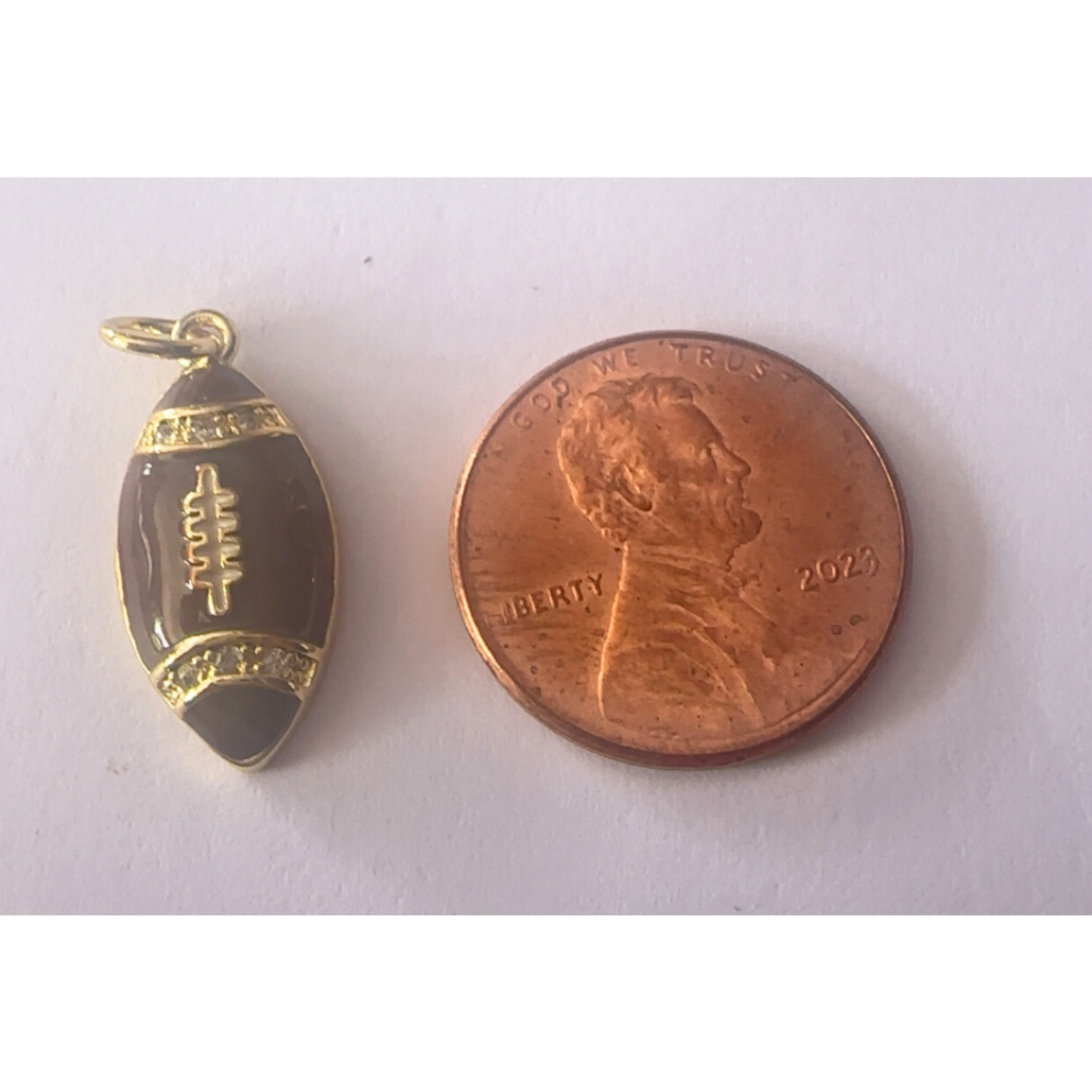 Gold football-shaped pendant next to a penny on a white background