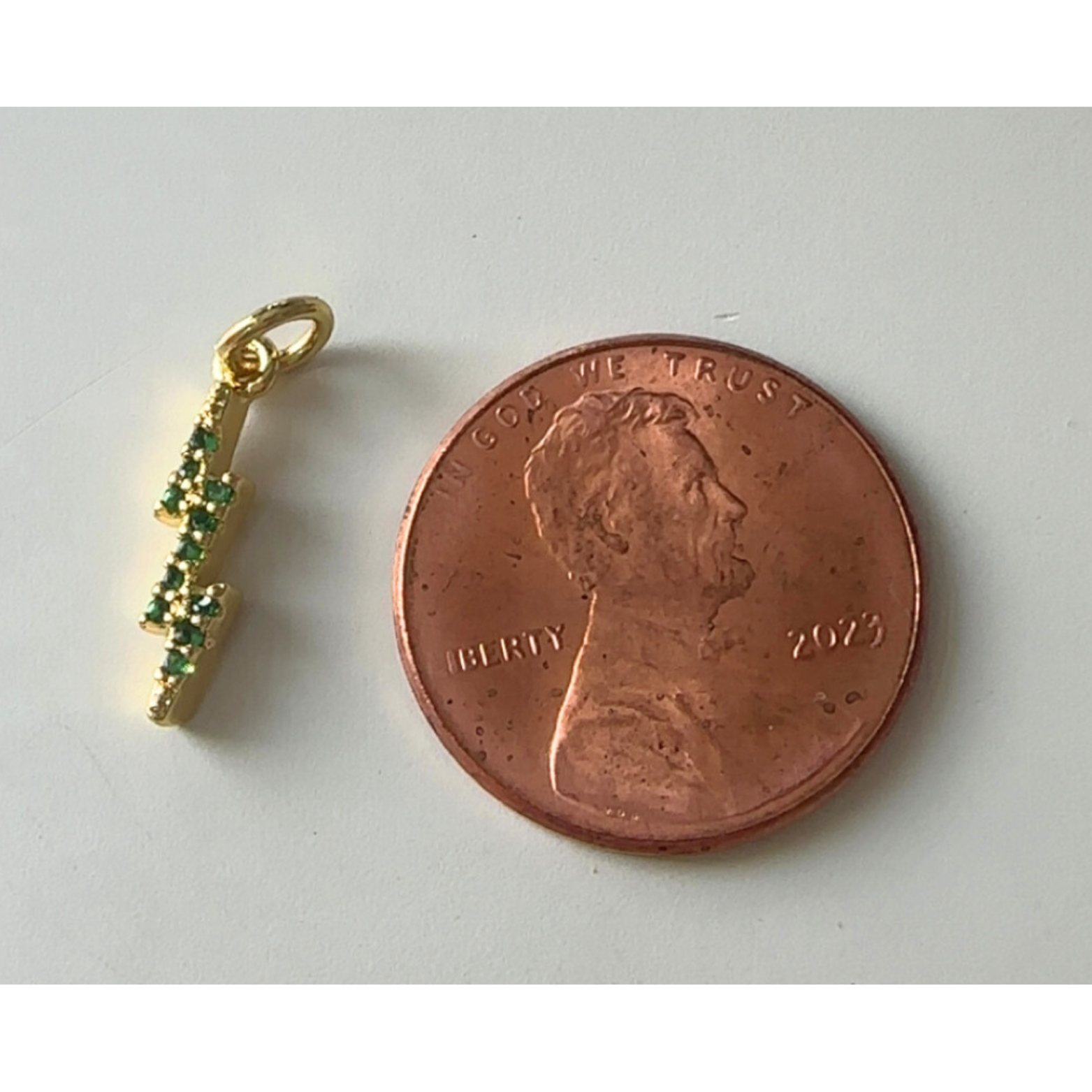 Gold pendant with green stones next to a penny on a white background