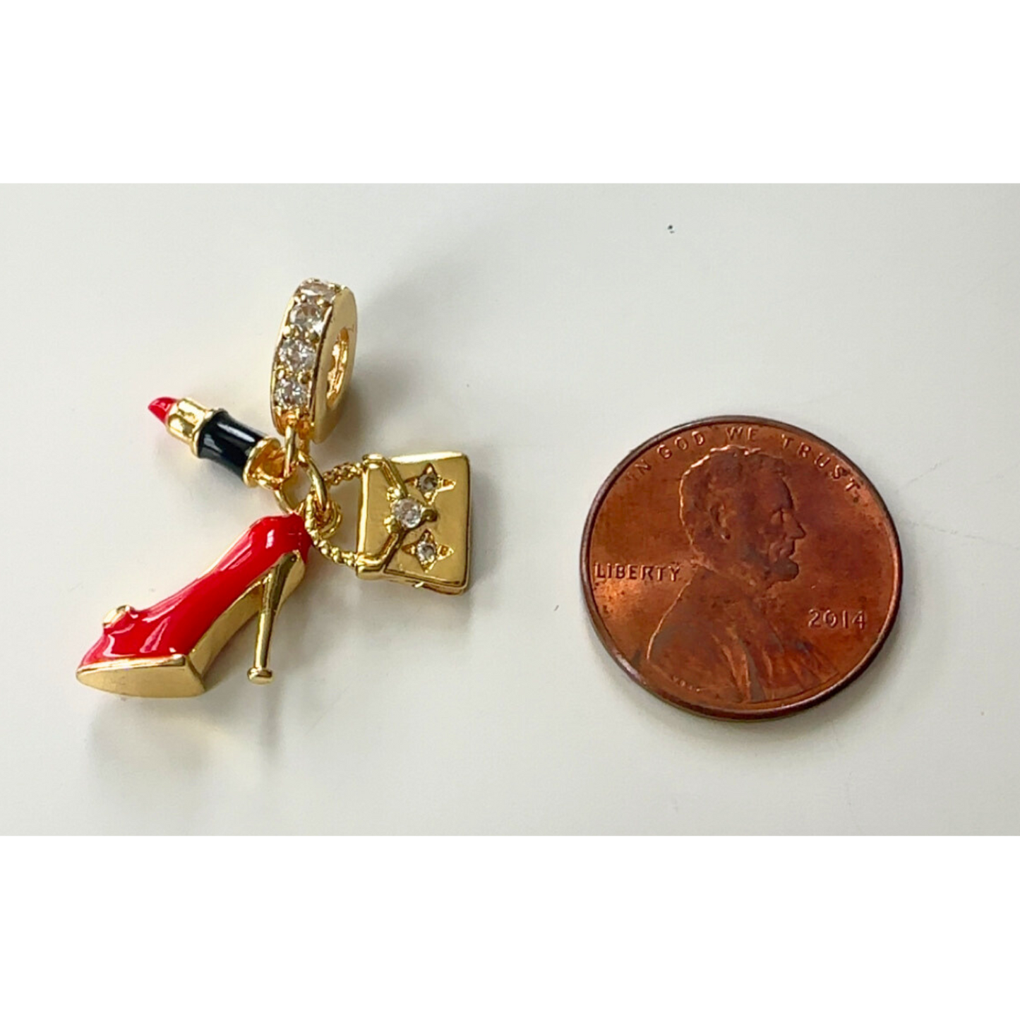 Gold charm with red high heel shoe and black lip gloss next to a penny on a white background